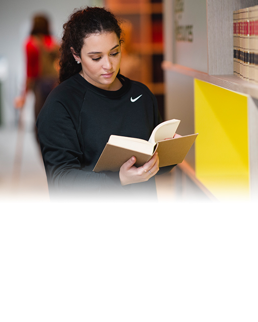 Female student standing in library reading book