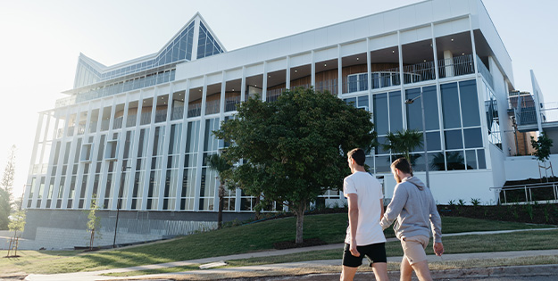 Two people walking outside a campus building. Grass and trees around.