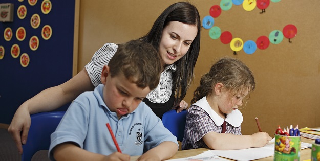 Female teacher helping two children at school desk