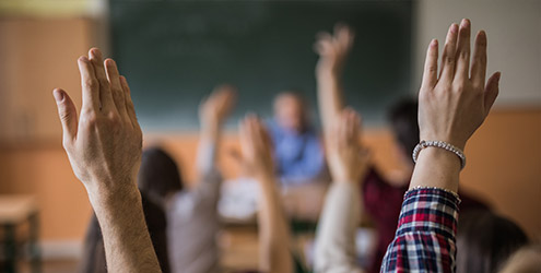 Teenagers putting their hands up in class to answer a question.