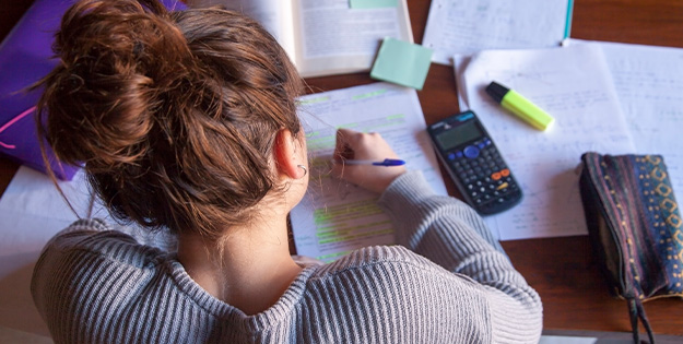 Teenage girl studying hard with calculator pens and workbooks.