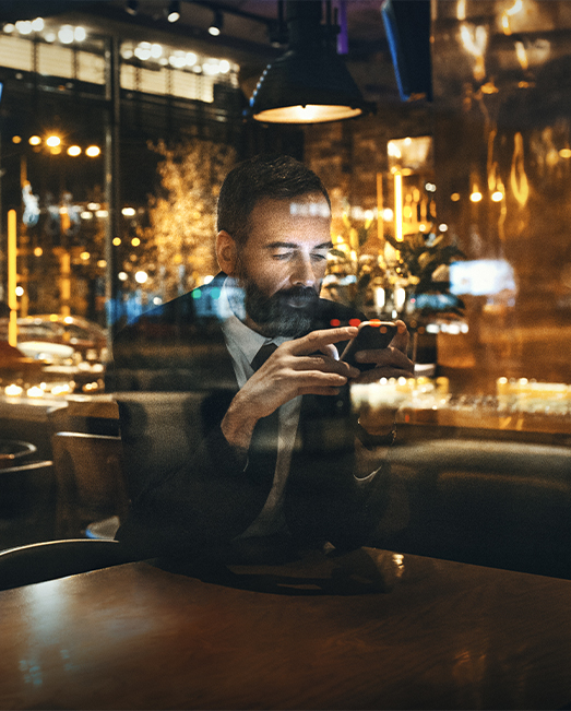 Man checking phone in cafe at night with lights reflected.