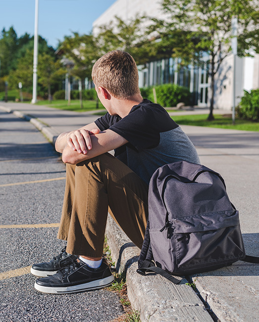 A teenage boy alone and waiting on a roadside curb.