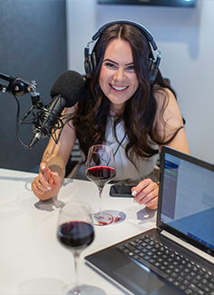 Victoria Devine sitting at a table with microphone, computer and red wine for podcast